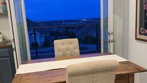 A dining area with a wooden table and chairs, a view of a residential area through an open door, and a framed picture on the wall. - Wine Country Guest House (Kennewick)
