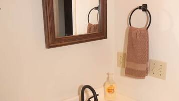 A bathroom with a white sink, a mirror with a wooden frame, a towel ring with a brown towel, and a soap dispenser.