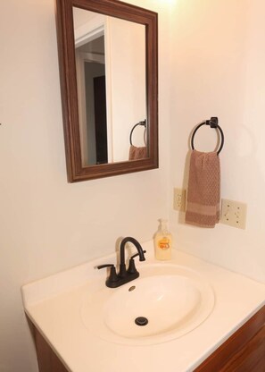 A bathroom with a white sink, a mirror with a wooden frame, a towel ring with a brown towel, and a soap dispenser.