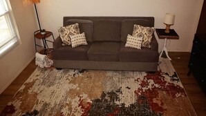Un salon avec un canapé marron, des coussins à motifs, un lampadaire et une petite table avec une lampe.