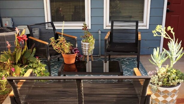 Une terrasse avec un banc en bois, deux chaises et des plantes en pot.