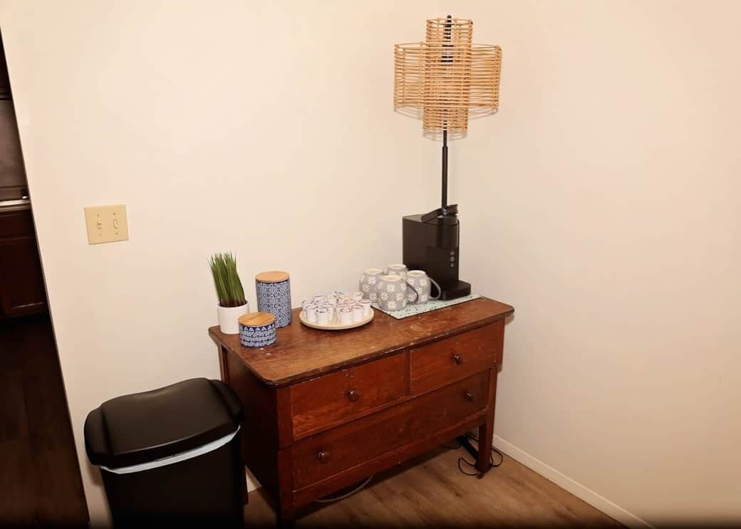 A wooden dresser with a lamp, a trash bin, and decorative items.