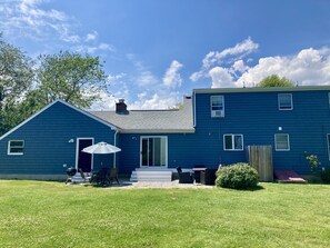 A two-story house with a blue exterior, a covered patio with outdoor furniture, and a small garden area.