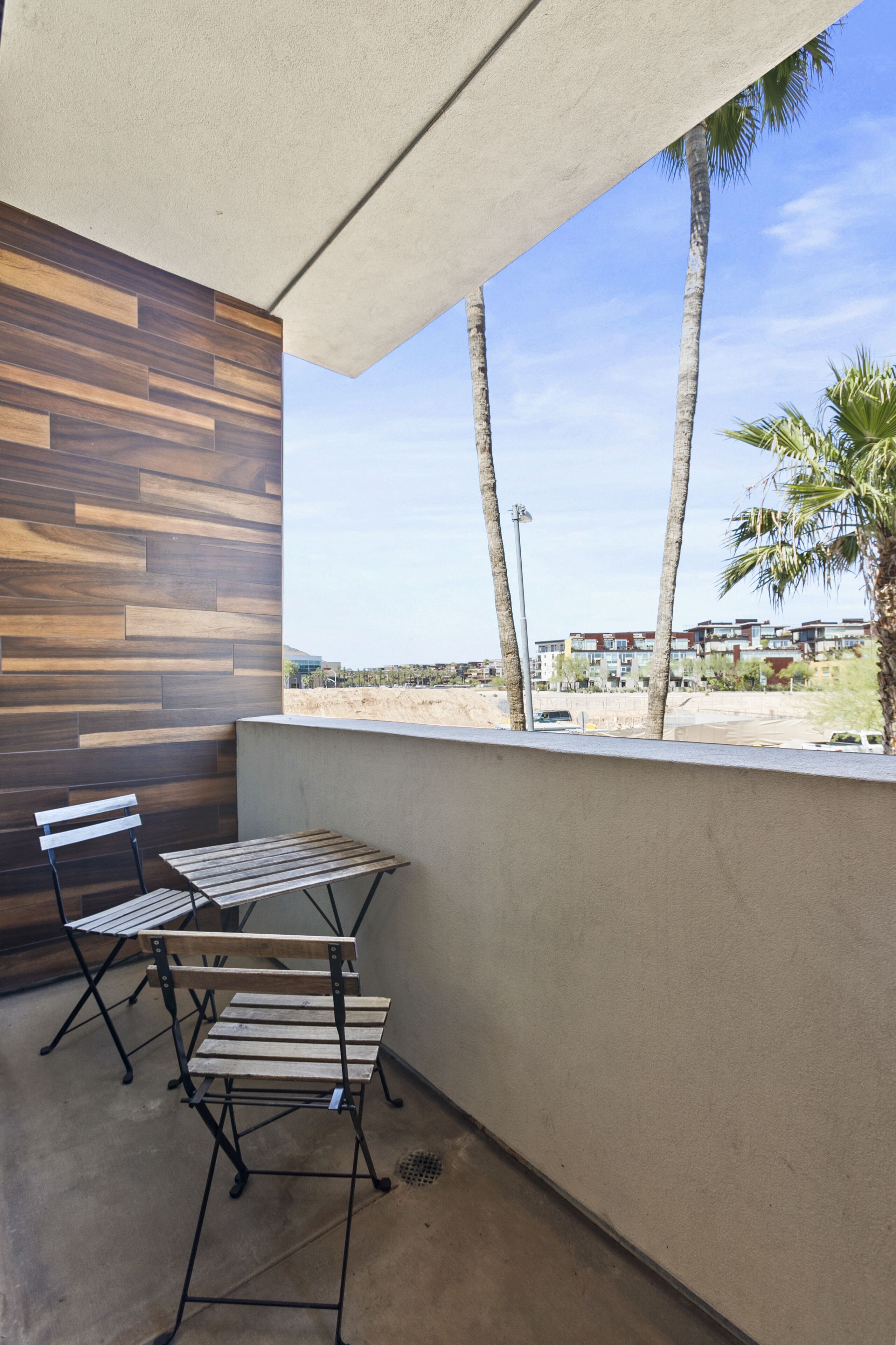 A balcony with a wooden wall, two metal chairs, and a table.