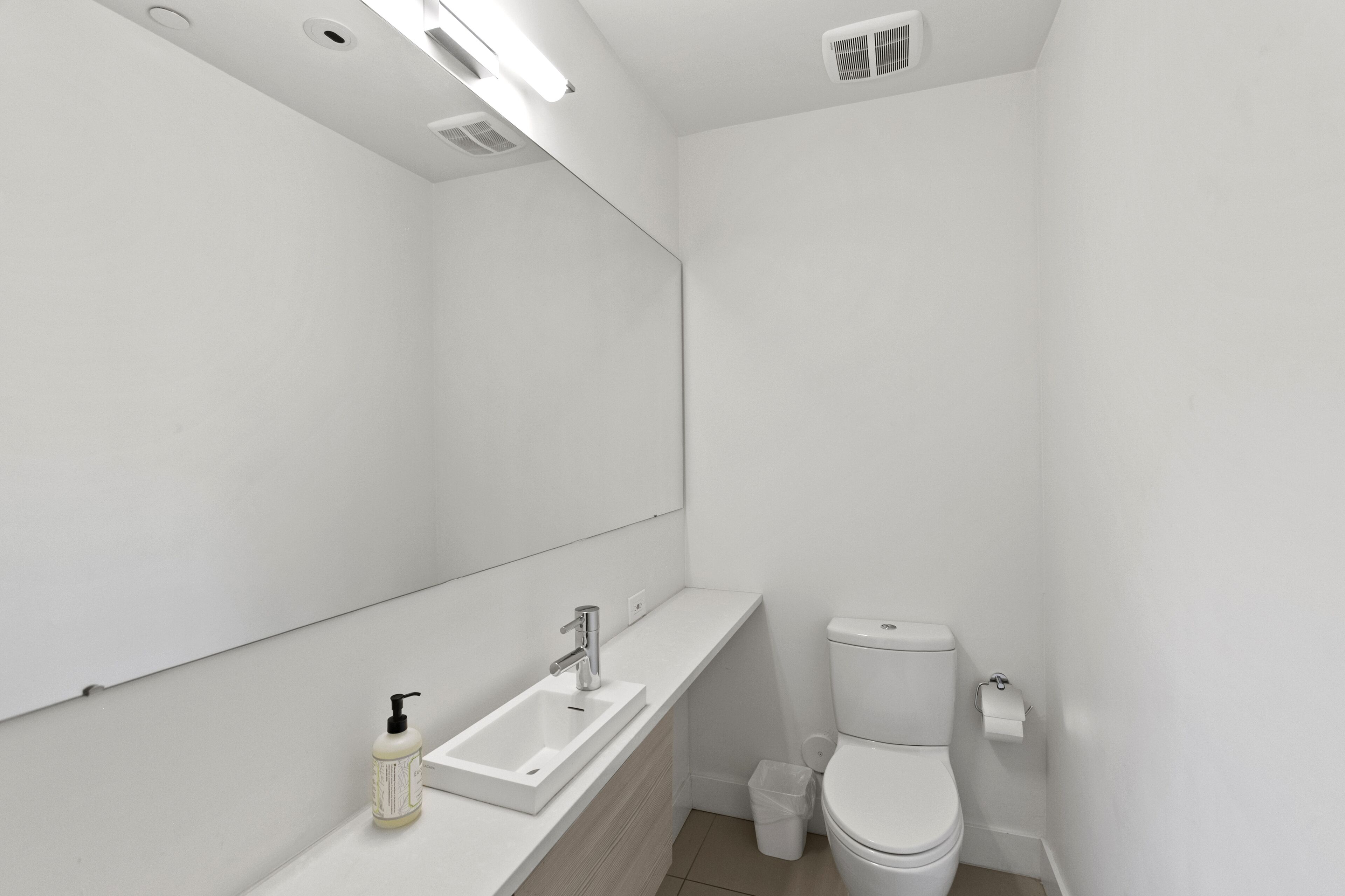 A modern bathroom with a white sink, mirror, and toilet.