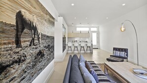 Una sala moderna con un cuadro abstracto grande, un sofá, una mesita de centro y una zona de comedor con taburetes de bar.