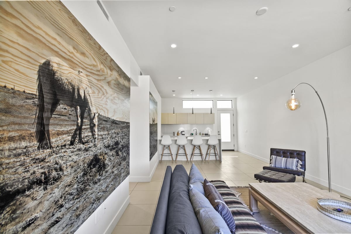 A modern living room with a large abstract painting, a sofa, a coffee table, and a dining area with bar stools.