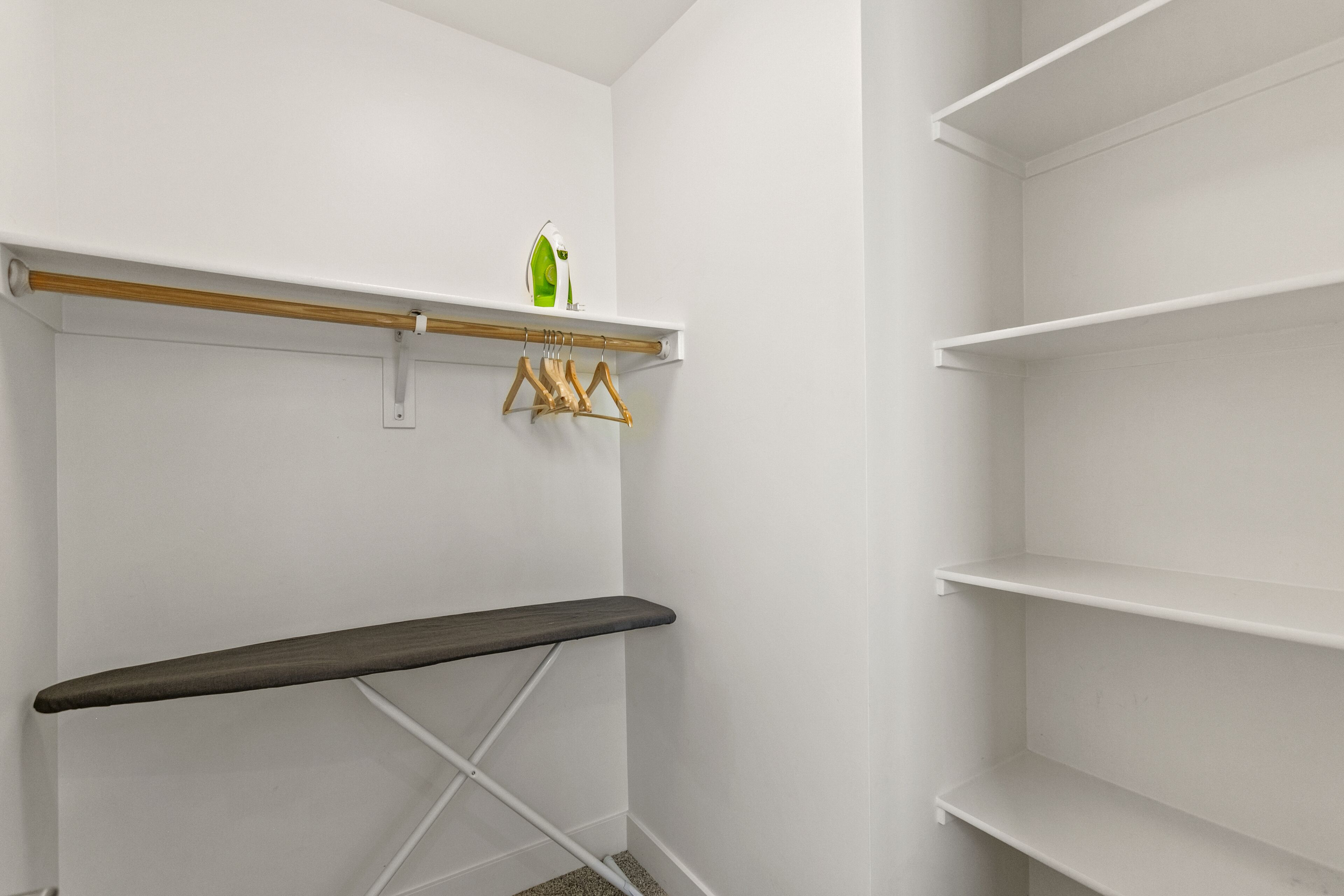 A white closet with a wooden bench, a hanging rack with clothes, and a shelf with a green bottle.