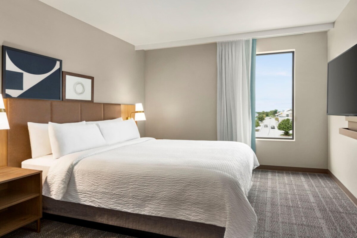 A hotel room with a bed, two bedside lamps, a nightstand, a TV, and a window with a view.