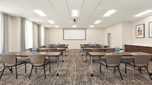 A conference room with a large screen, multiple tables, chairs, and water bottles. - Staybridge Suites Lexington S Medical Ctr Area (Lexington)