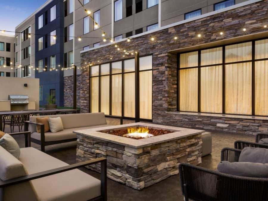An outdoor patio area with a stone fire pit, seating, and string lights.