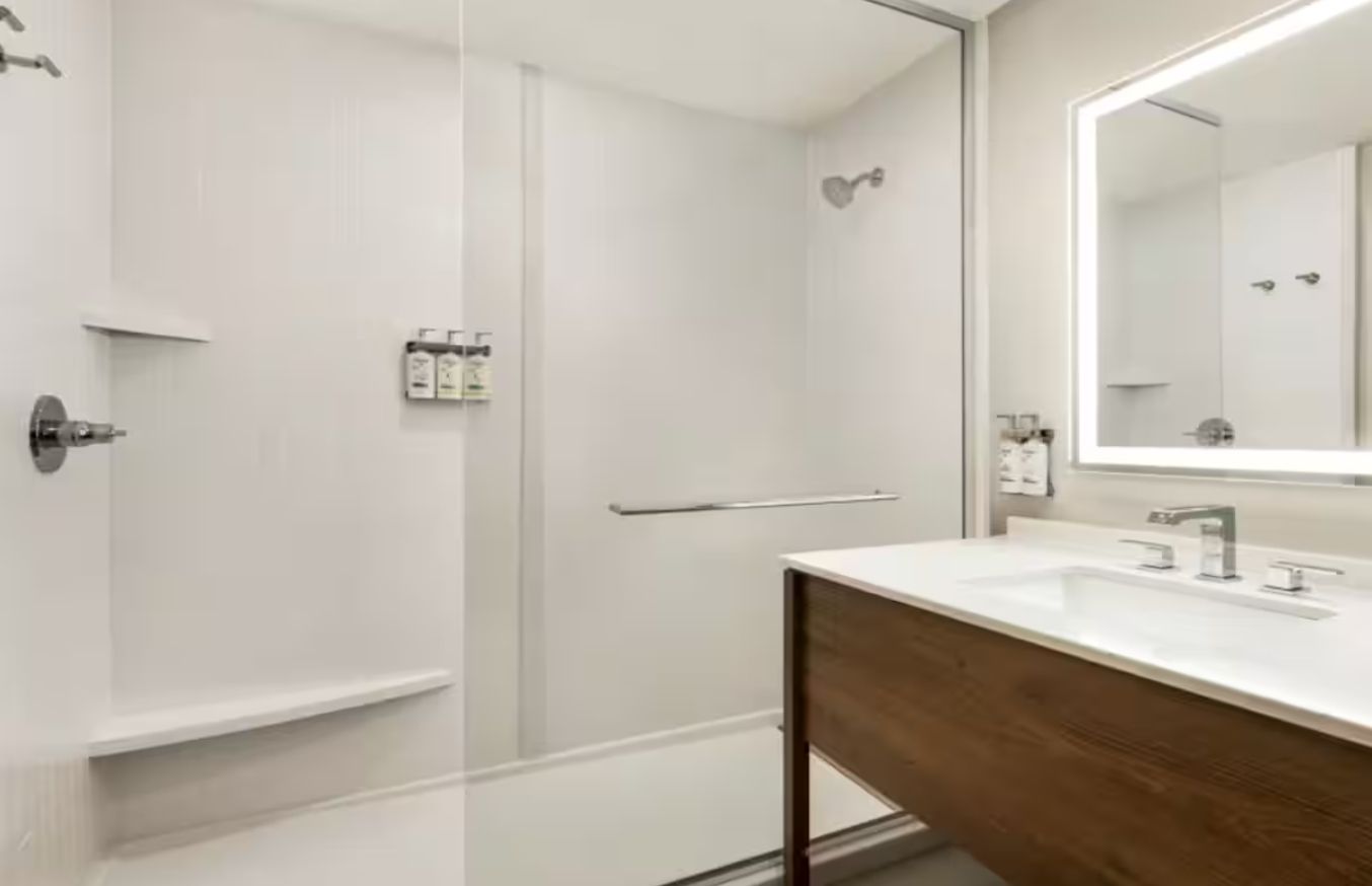 Un baño moderno con cabina de ducha de vidrio, tocador de madera y un espejo grande.