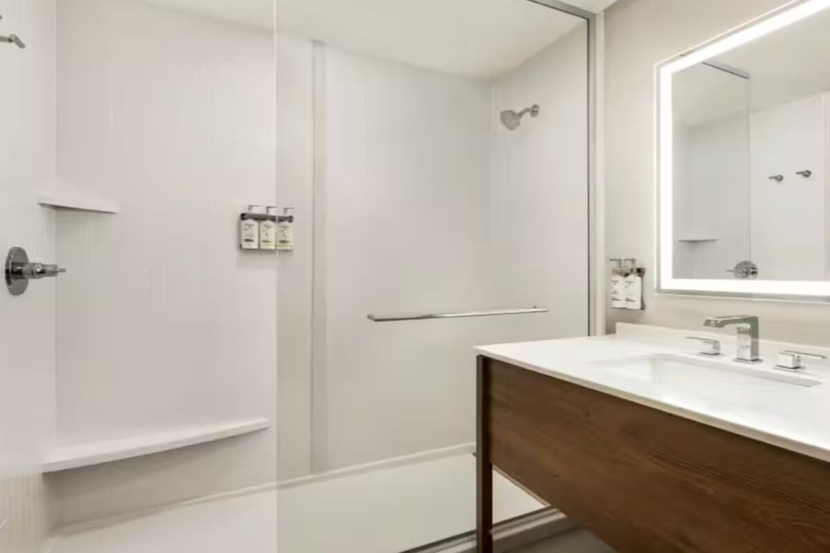 A modern bathroom with a glass shower enclosure, a wooden vanity, and a large mirror.