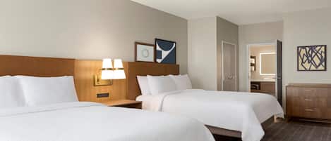 A hotel room with two beds, a nightstand with lamps, a door, a bathroom mirror, and a dresser.