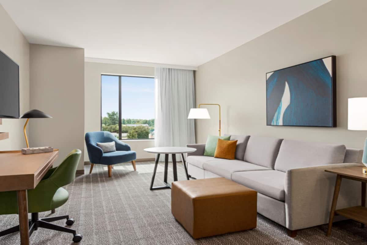 A hotel room with a sofa, armchair, desk, and a TV.