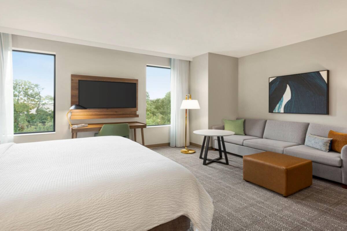 A hotel room with a large bed, a sofa, a small table, a TV, and a painting on the wall.