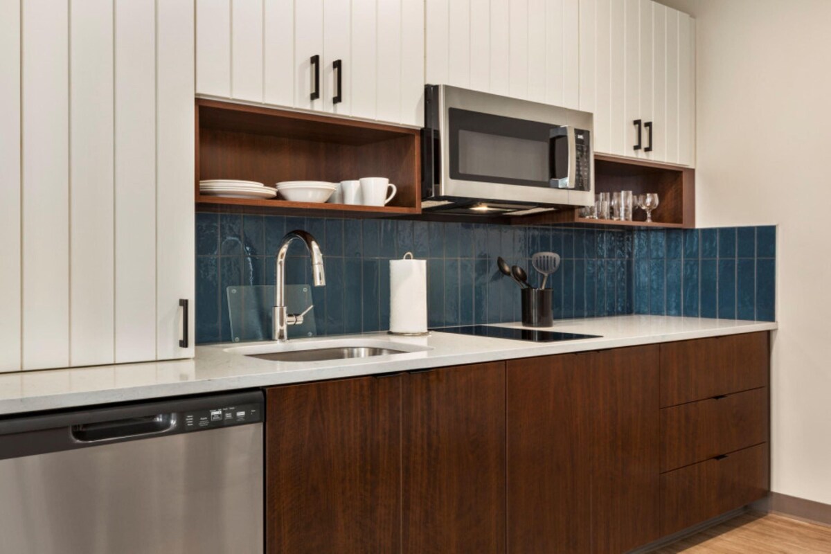 A modern kitchen with white cabinets, a stainless steel dishwasher, a microwave, and a blue tiled backsplash.