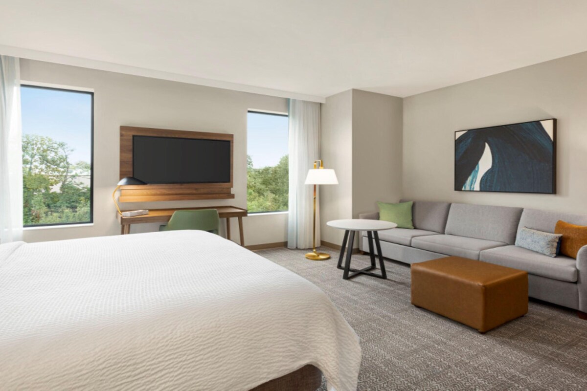 A hotel room with a large bed, a sofa, a small table, a TV, and a painting on the wall.