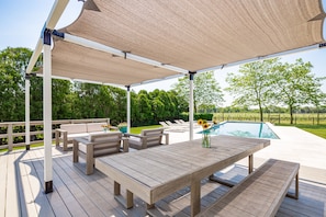 En täckt uteplats med en pool, trädgårdsmöbler och utsikt över den omgivande grönskan.