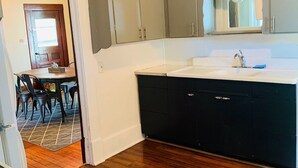 Una cocina con armarios grises, encimera blanca y suelo de madera.
