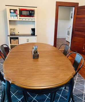 Un comedor con una mesa redonda de madera, sillas, un microondas y una cafetera sobre un mueble.