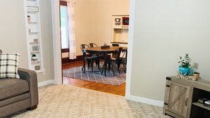 Una sala de estar con un sofá marrón, un comedor con una mesa y sillas, y una cocina visible a través de un arco.
