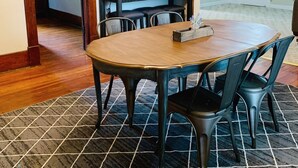 Un comedor con una mesa y sillas de madera, un tapete estampado y una puerta que da a otra habitación.