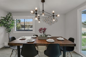 Un comedor con mesa de madera, sillas negras, una lámpara moderna y vistas al exterior.