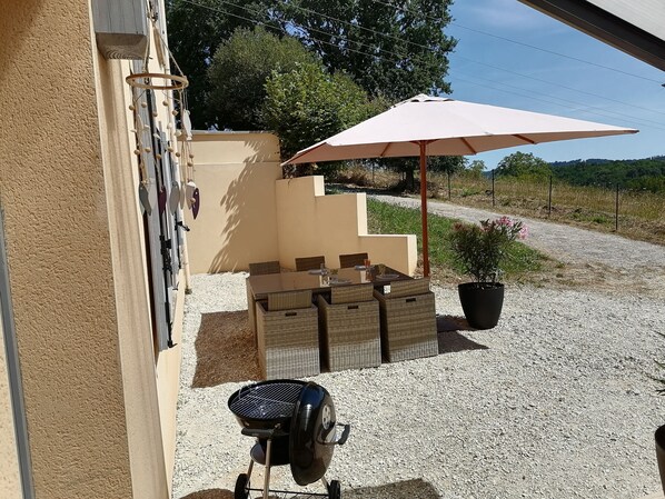 An outdoor patio with a barbecue grill, a table with chairs, and a large umbrella.