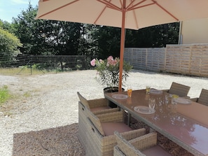 Un área de comedor al aire libre con mobiliario de mimbre y un paraguas grande.