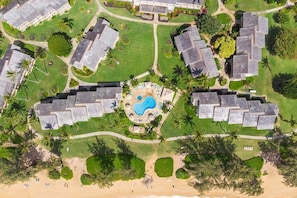 Vista aérea de um resort com vários edifícios, uma área de piscina central e vegetação ao redor.