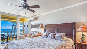 A bedroom with a large bed, a ceiling fan, a nightstand with a lamp, and a view of the ocean through a sliding door. - View Beachfront, Split AC, Pool Hot Tub, King Bed (Kapaa)