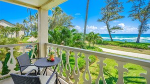 Un balcone con mobili in vimini e un tavolo, con vista su una spiaggia, palme e onde dell'oceano.