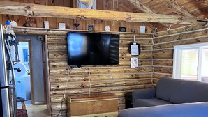 Interior acogedor de una cabaña con techo de madera, un televisor plano de pantalla montado, un sofá azul y un aparador de madera.