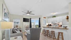 A modern kitchen with white cabinets, a microwave, and a coffee maker. There is a dining area with a gray armchair and a table. - Gulf Shores Plantation-Dunes 5107 (Gulf Shores)