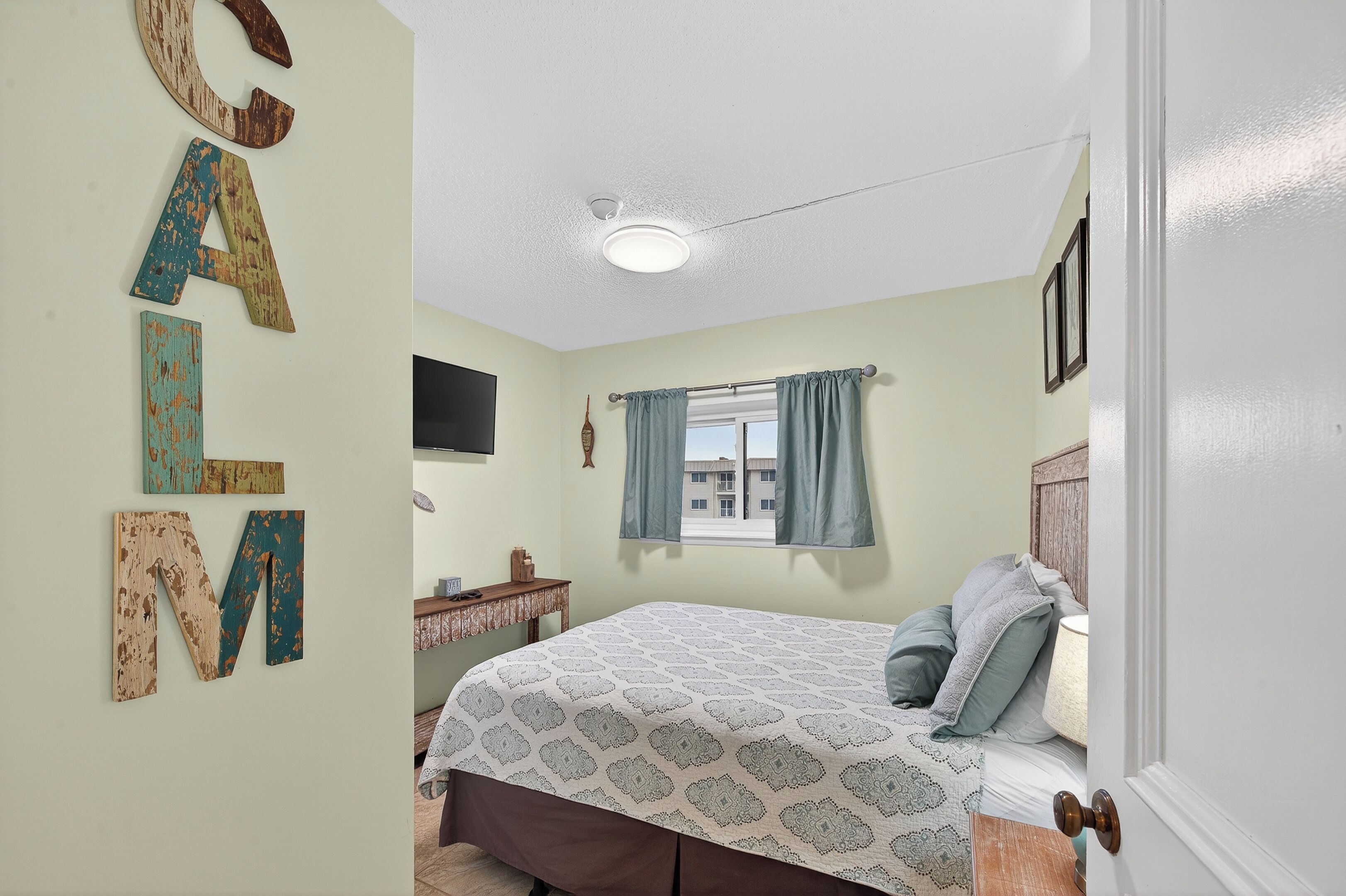 A bedroom with a bed, a desk, a window with curtains, and wall decorations.