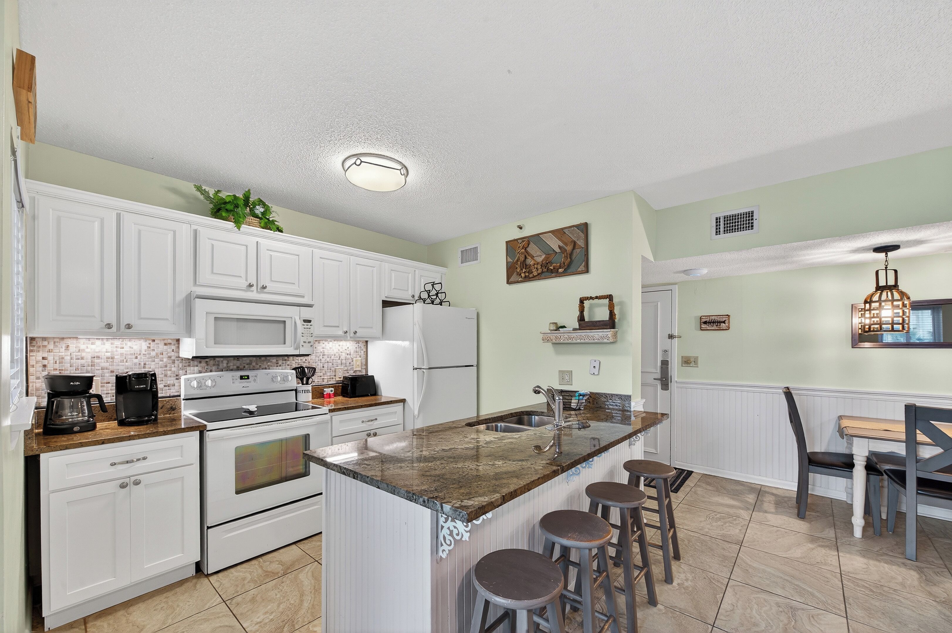 A modern kitchen with white cabinets, a granite countertop, and a central island with bar stools.