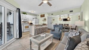 A spacious living area with a ceiling fan, a dining table, and a kitchen area with white cabinets and a microwave. - Gulf Shores Plantation-Dunes 5107 (Gulf Shores)
