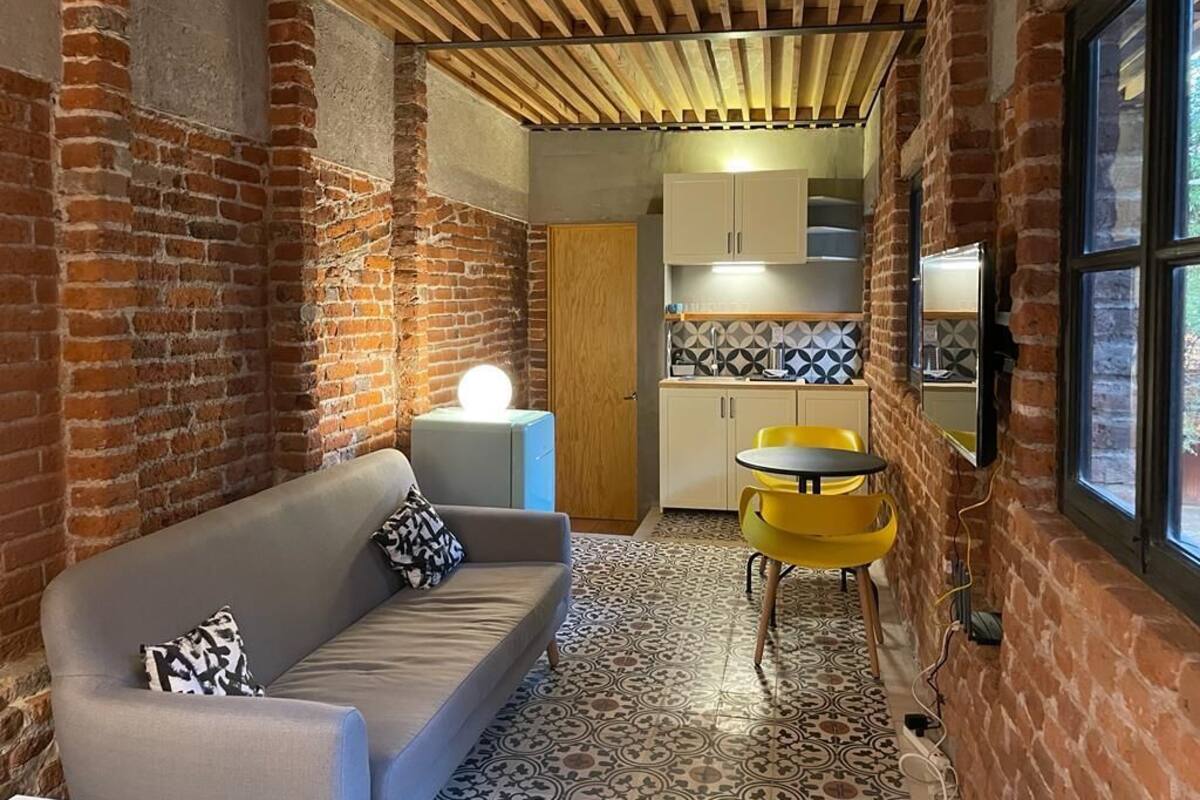 Una habitación acogedora con sofá, una mesita y una zona de cocina con armarios y salpicadero de azulejos.