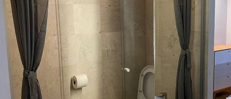 A modern bathroom with a glass shower enclosure, two toilets, a wooden vanity with a sink, and a mirror.