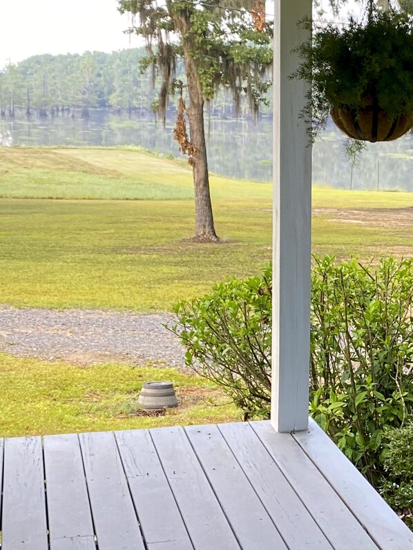 A wooden deck with a hanging planter, a tree, and a grassy field in the background.