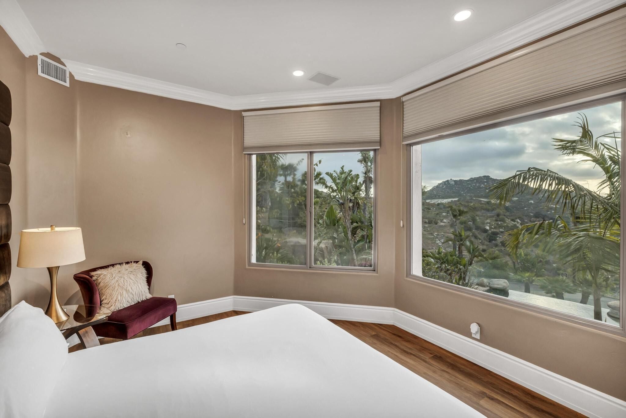 A bedroom with a large window, a bed, a chair, and a lamp.