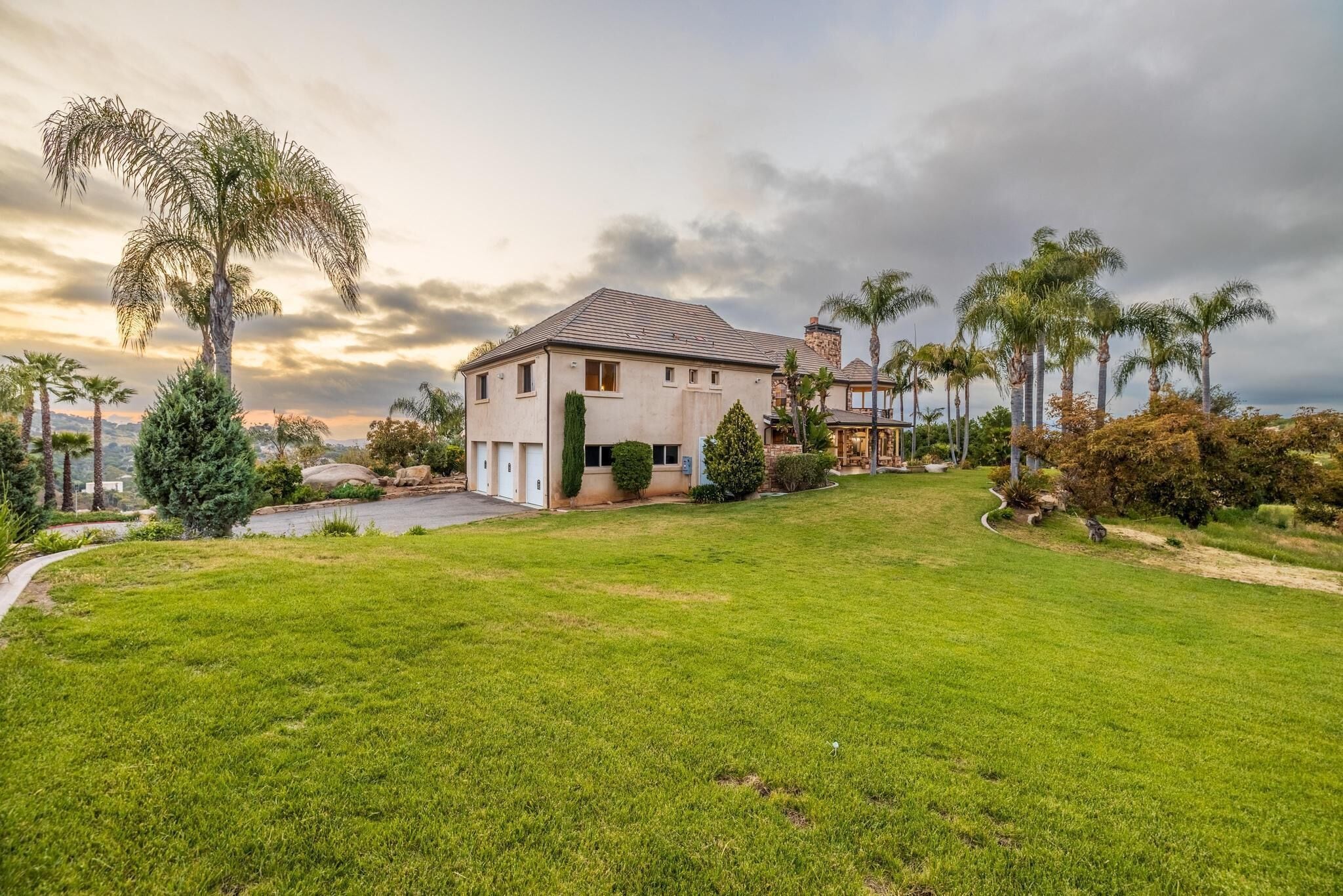 A large house with a well-maintained lawn, palm trees, and a view of the ocean.