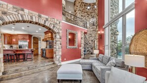 Un'ampia zona giorno con un arco in pietra che conduce a una cucina, una scala e un'ampia finestra con vista sull'esterno.