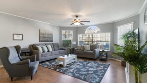 A spacious living room with two grey sofas, a white coffee table, and a large window providing natural light.