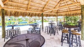 A covered outdoor area with tables and chairs, a pool in the background, and a thatched roof structure. - Storey Lake Resort, Private Pool, Near Famous Attractions!! (Kissimmee)