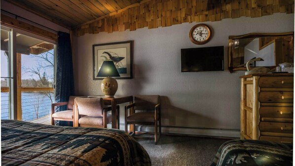 A room with a bed, two chairs, a desk, a lamp, a television, and a wooden dresser.