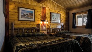 Una habitación tipo cabaña de troncos con dos camas, paredes de madera, cuadros enmarcados y una ventana con cortinas.