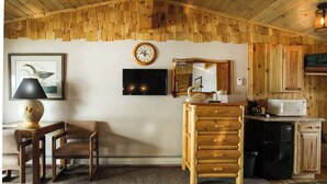 Una habitación acogedora con techo de madera, televisor, reloj, espejo, armario de madera, microondas y refrigerador.