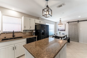 A modern kitchen with white cabinets, a granite countertop, a black refrigerator, and a hanging light fixture.